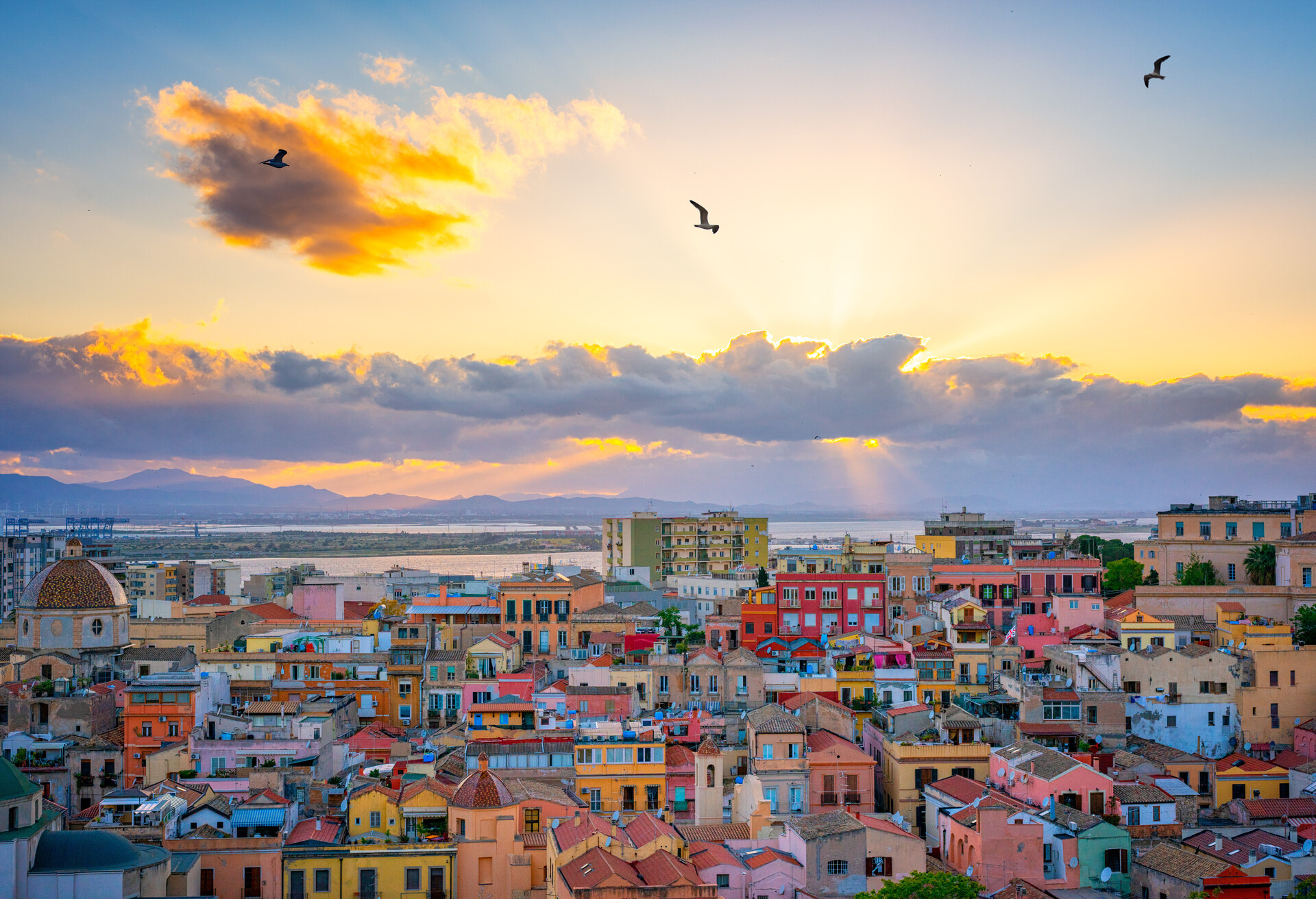 Sunset on Cagliari, panorama of the old city center with traditional colored houses with beautiful yellow-pink clouds and seagull's in the sky, Sardinia Island, Italy; Shutterstock ID 1095569708; Purpose: Destiny; Brand (KAYAK, Momondo, Any): Any